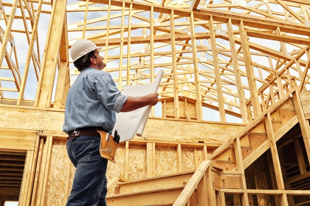 A man holding papers in front of a wooden structure.